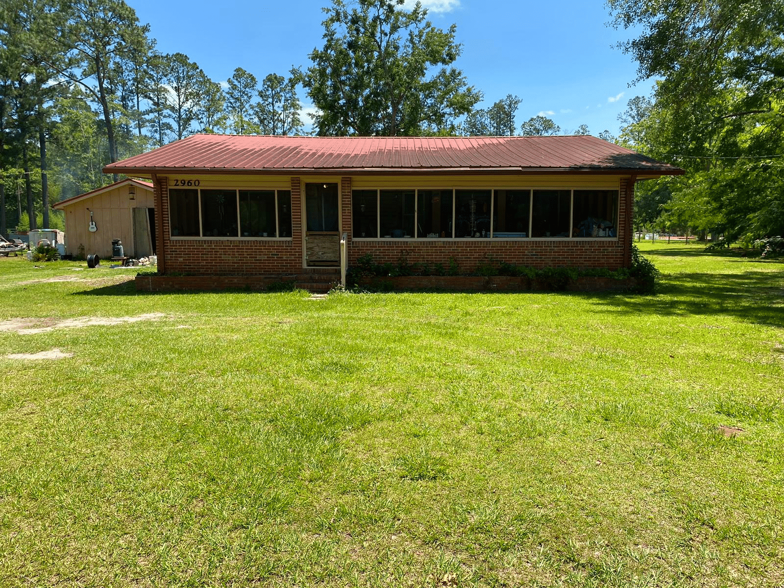 Well-maintained brick home at 2960 Co Rd 381, Wewahitchka, FL featuring a spacious lawn and large front porch under a red roof, surrounded by lush greenery.